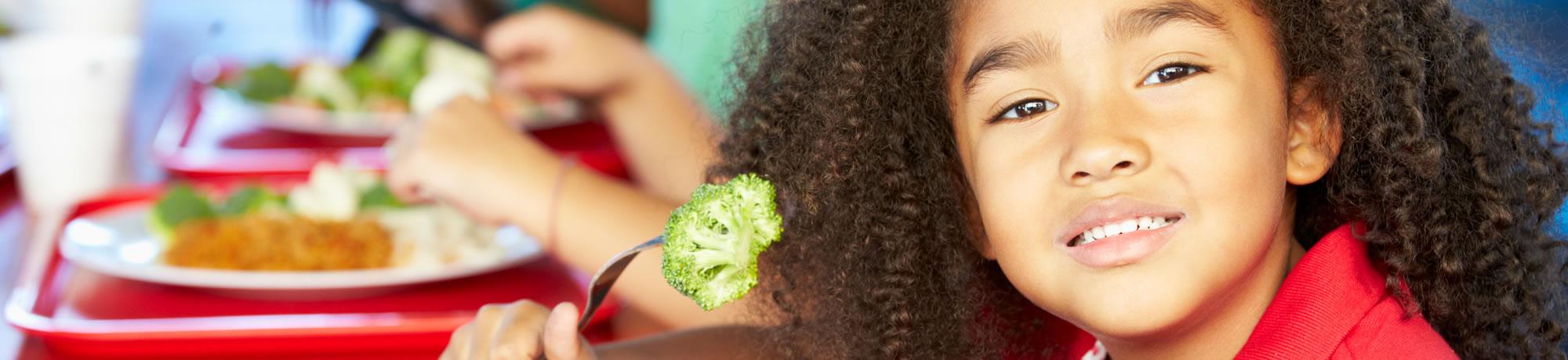 Girl holding broccoli with fork.